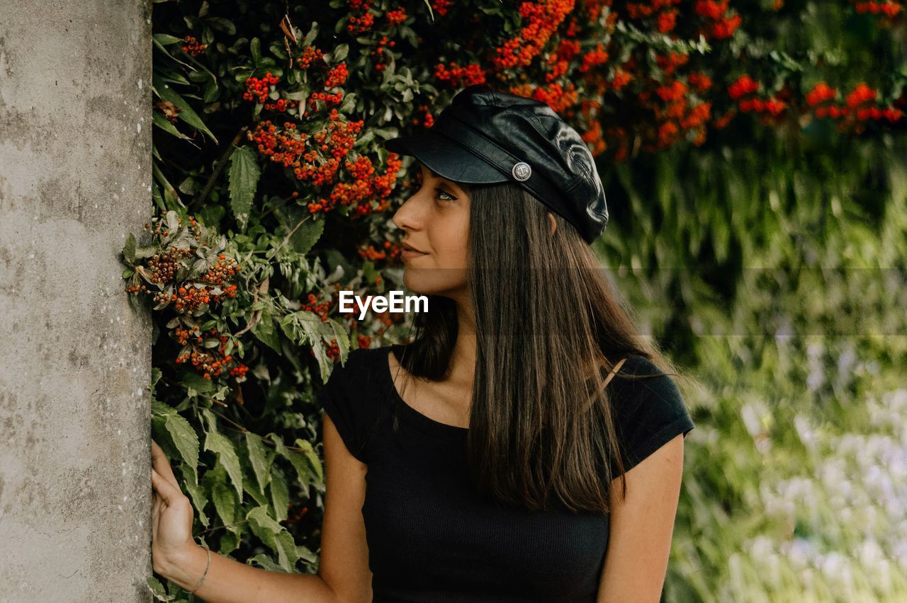 Woman in cap looking away against flowering plants
