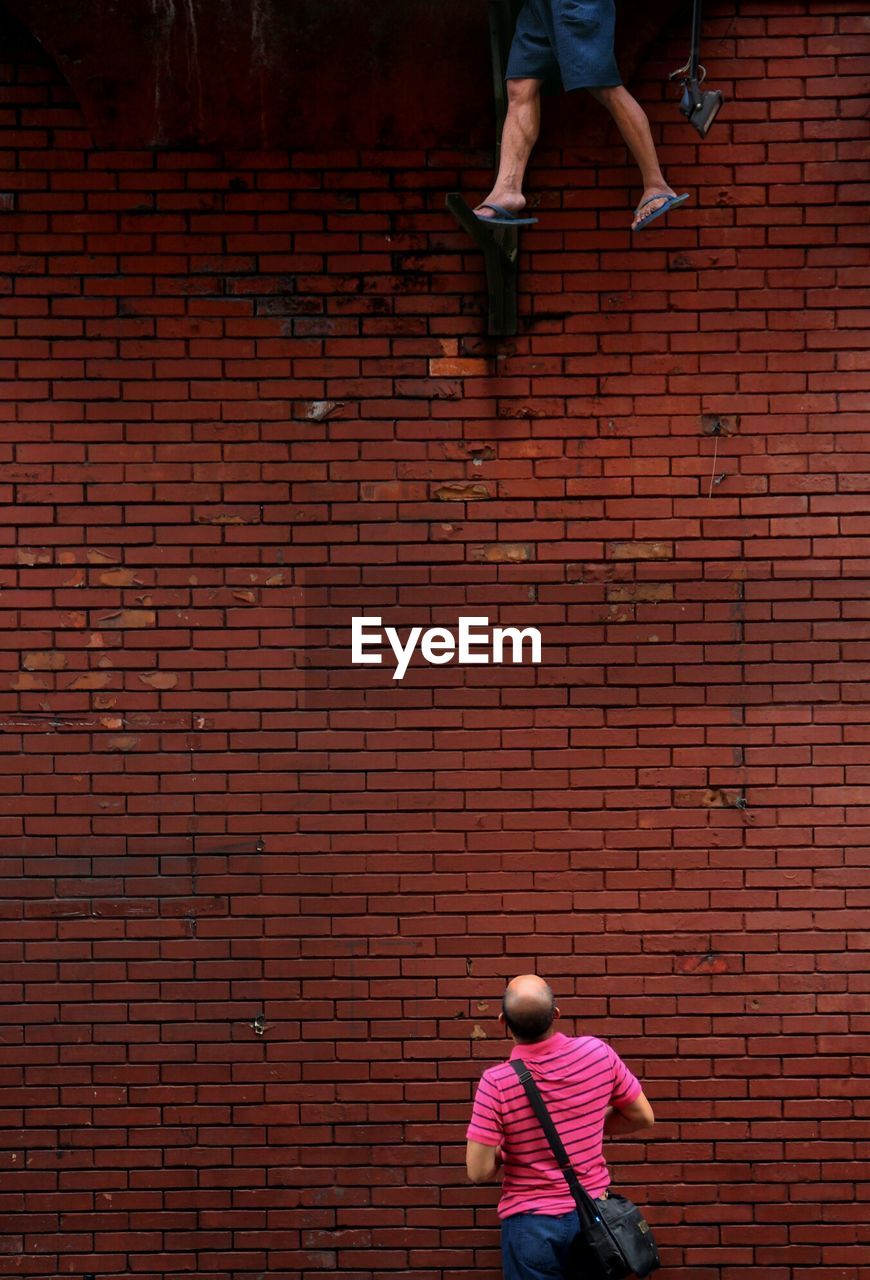 Rear view of man looking at person standing against wall