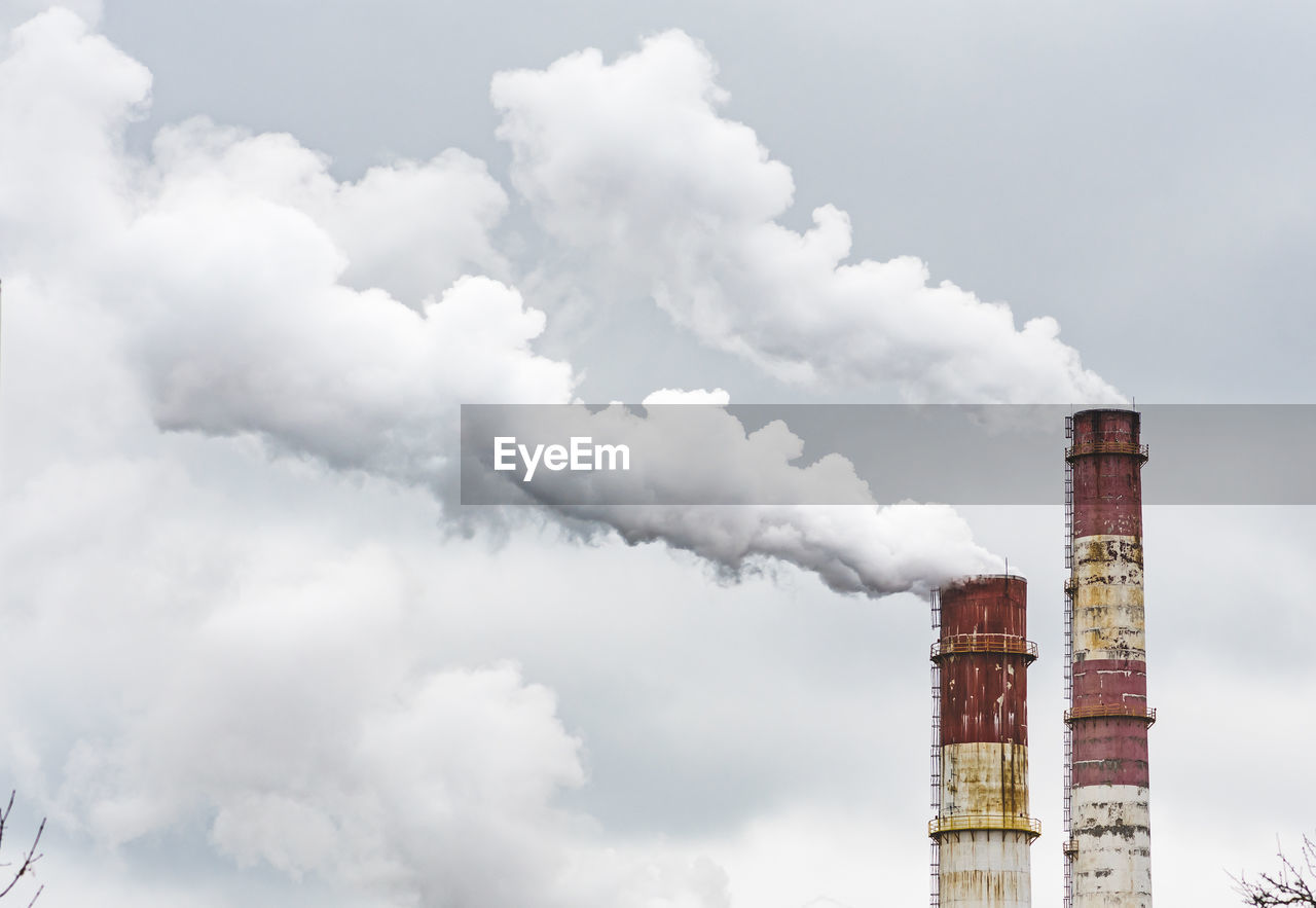 Thick white smoke from industrial factory old rusty chimneys on a cloudy grey sky background