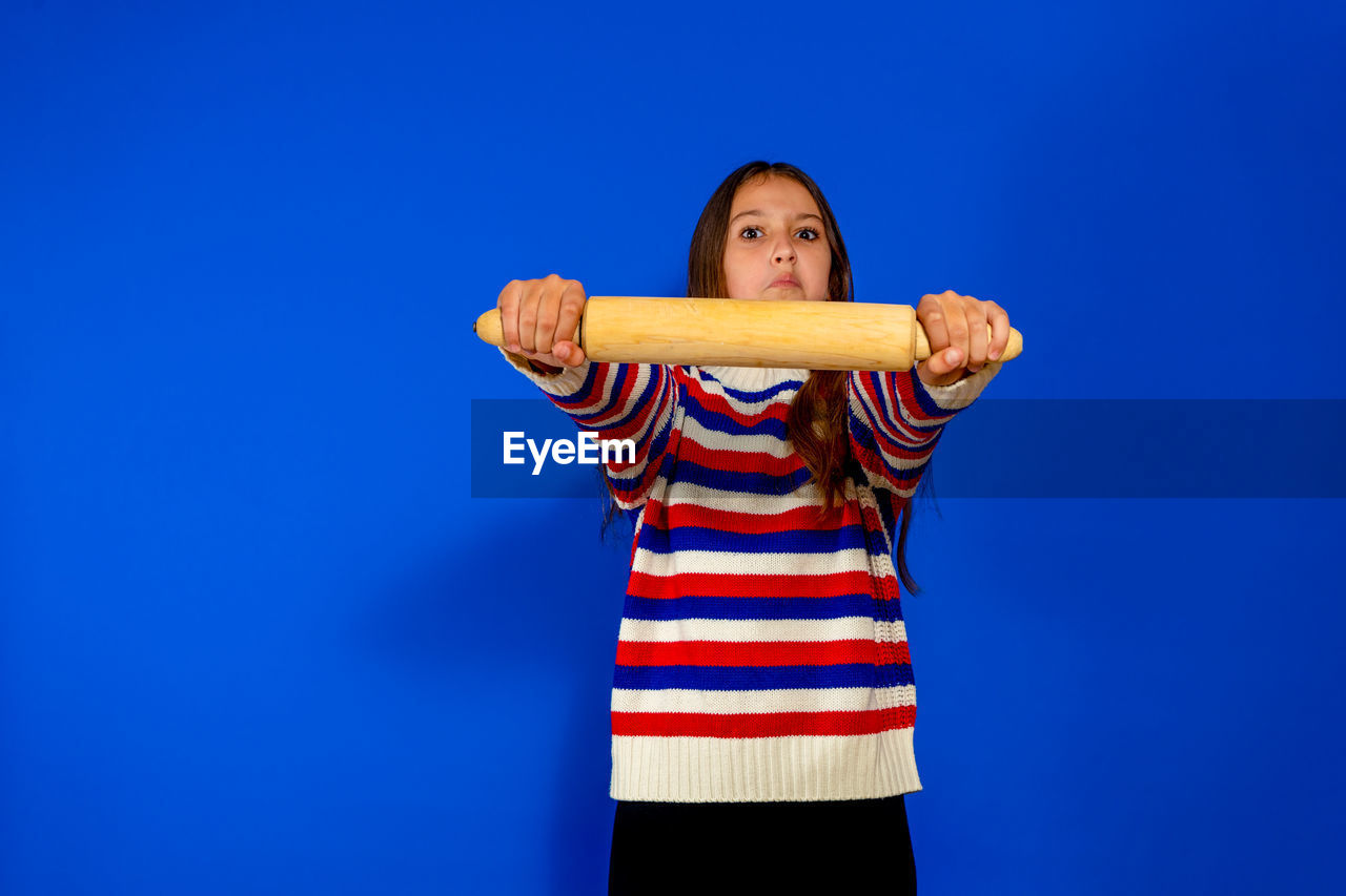 blue, one person, studio shot, colored background, striped, blue background, portrait, copy space, indoors, front view, standing, emotion, looking at camera, child, childhood, women, waist up, adult, casual clothing, clothing, performing arts, young adult, person, happiness, arm, limb, female, fun, holding, smiling, cut out