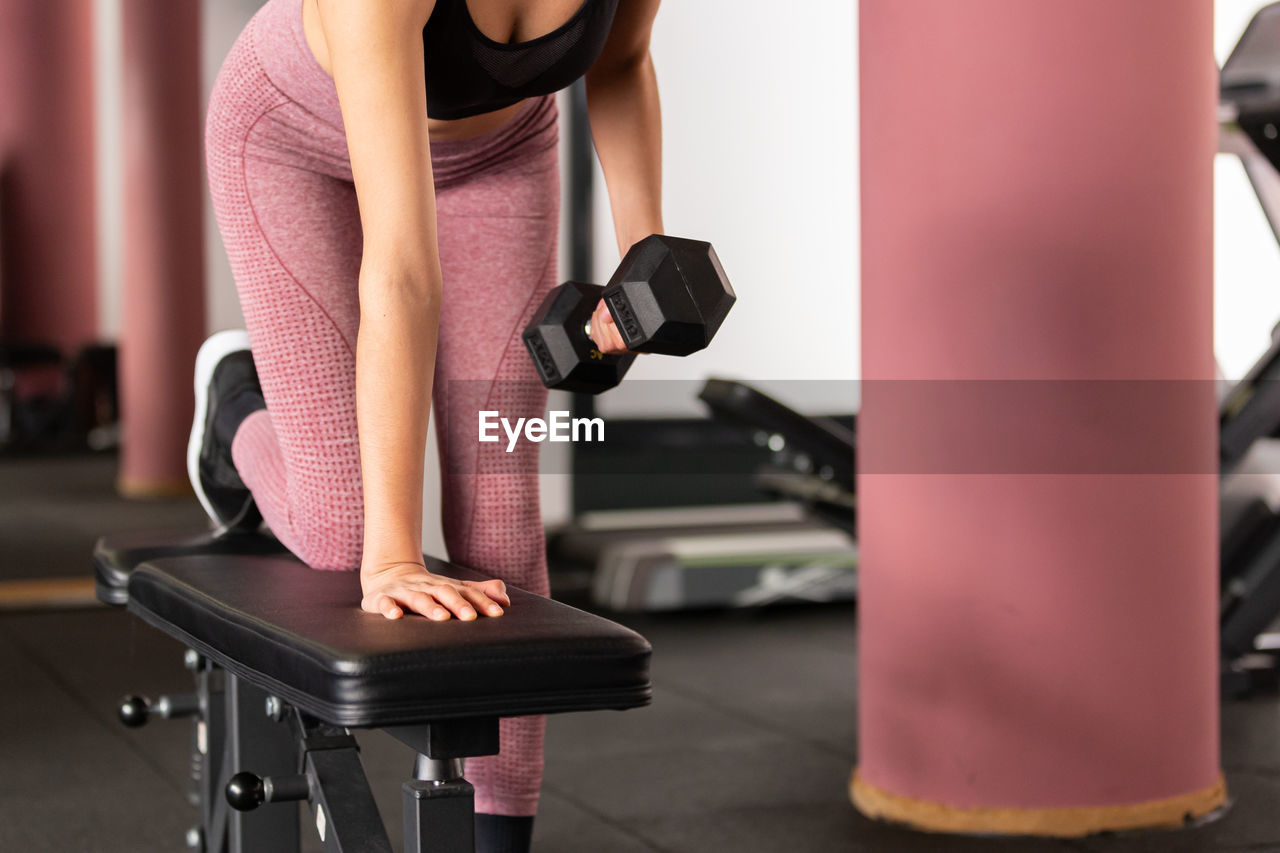 rear view of woman exercising with dumbbell in gym