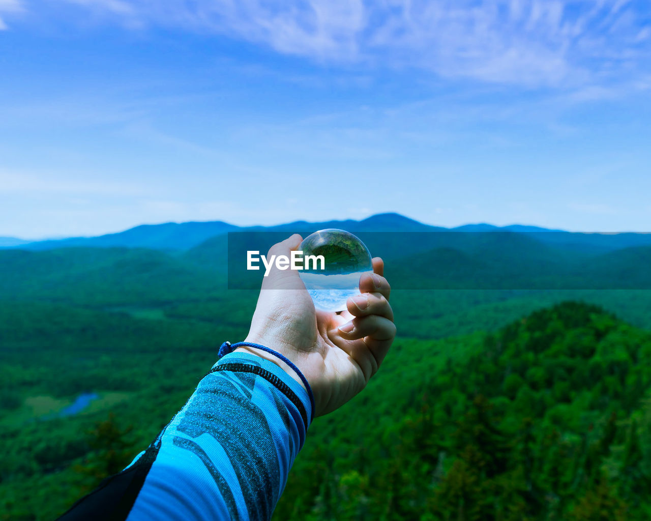 Cropped image of person holding crystal ball against mountains 