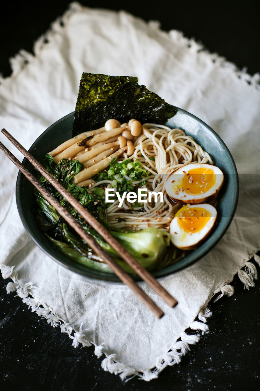 From above of ceramic bowl with delicious ramen and chopsticks placed on table covered with white tablecloth