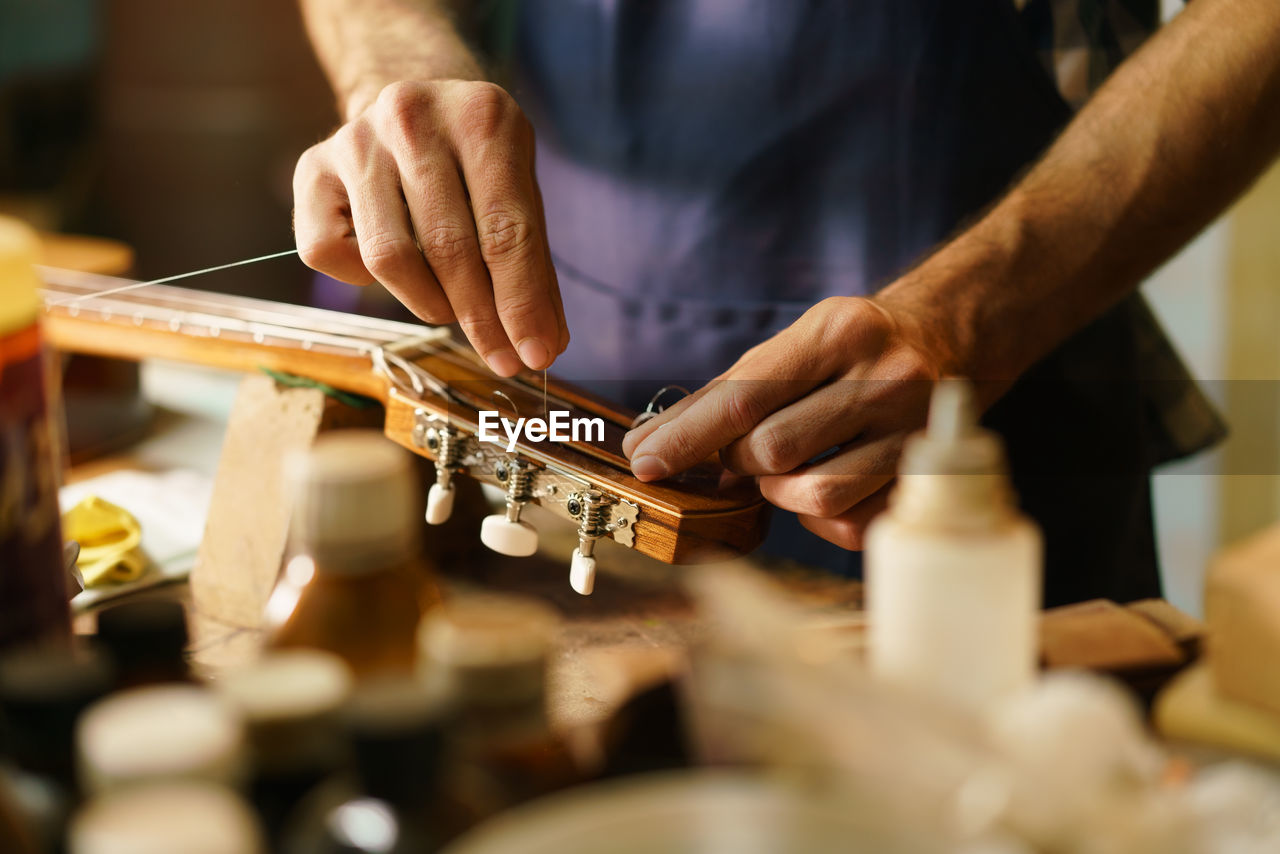 Midsection of man preparing guitar in workshop