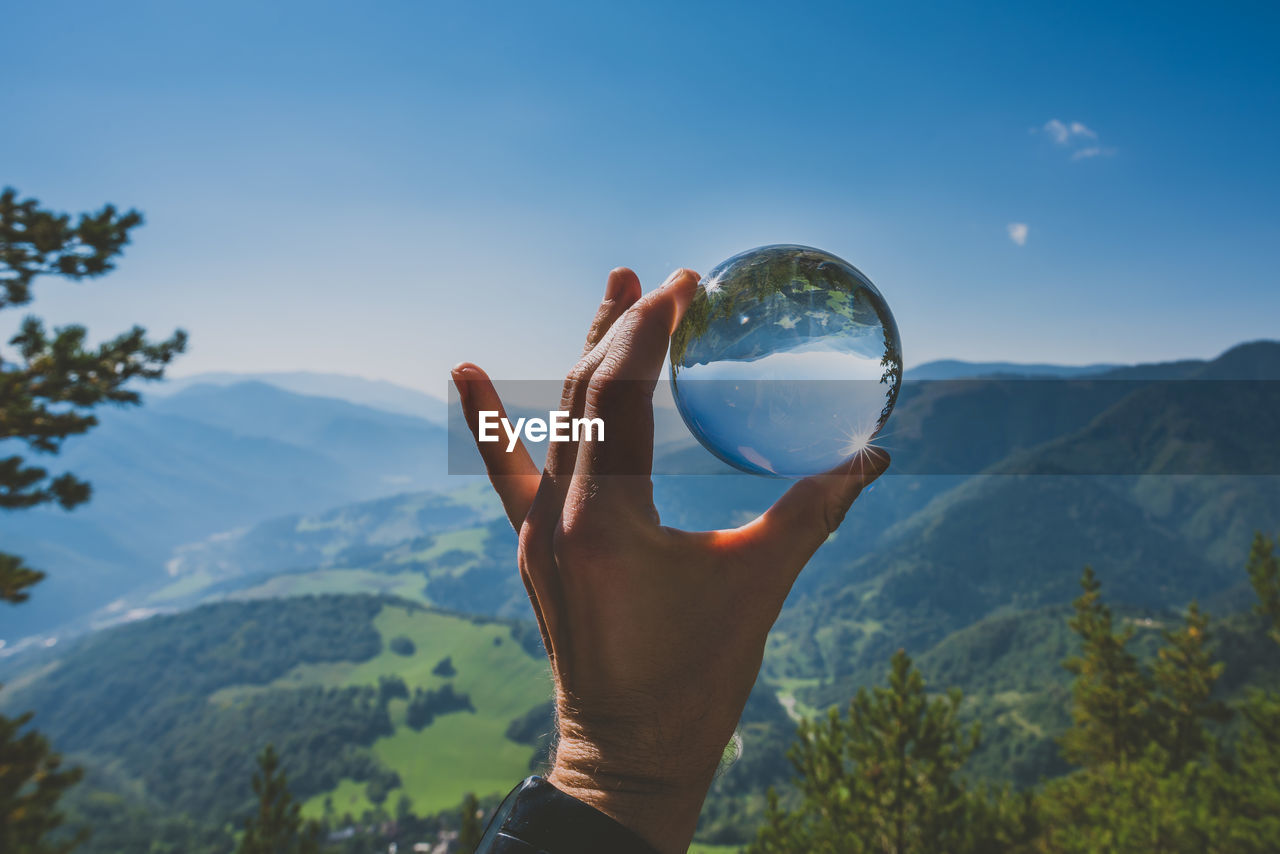Cropped hand holding crystal ball against mountains