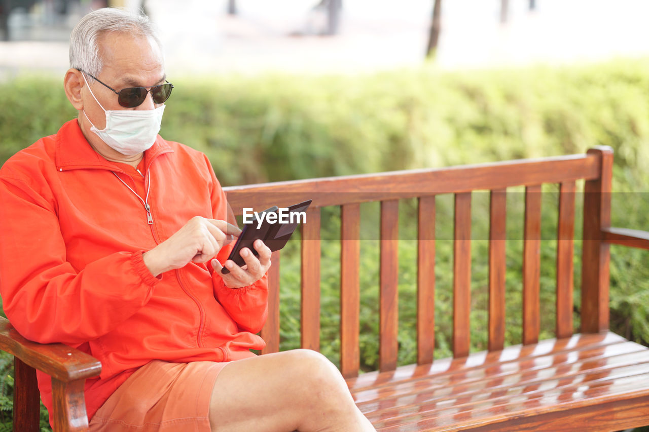 Senior man wearing mask using mobile phone outdoors