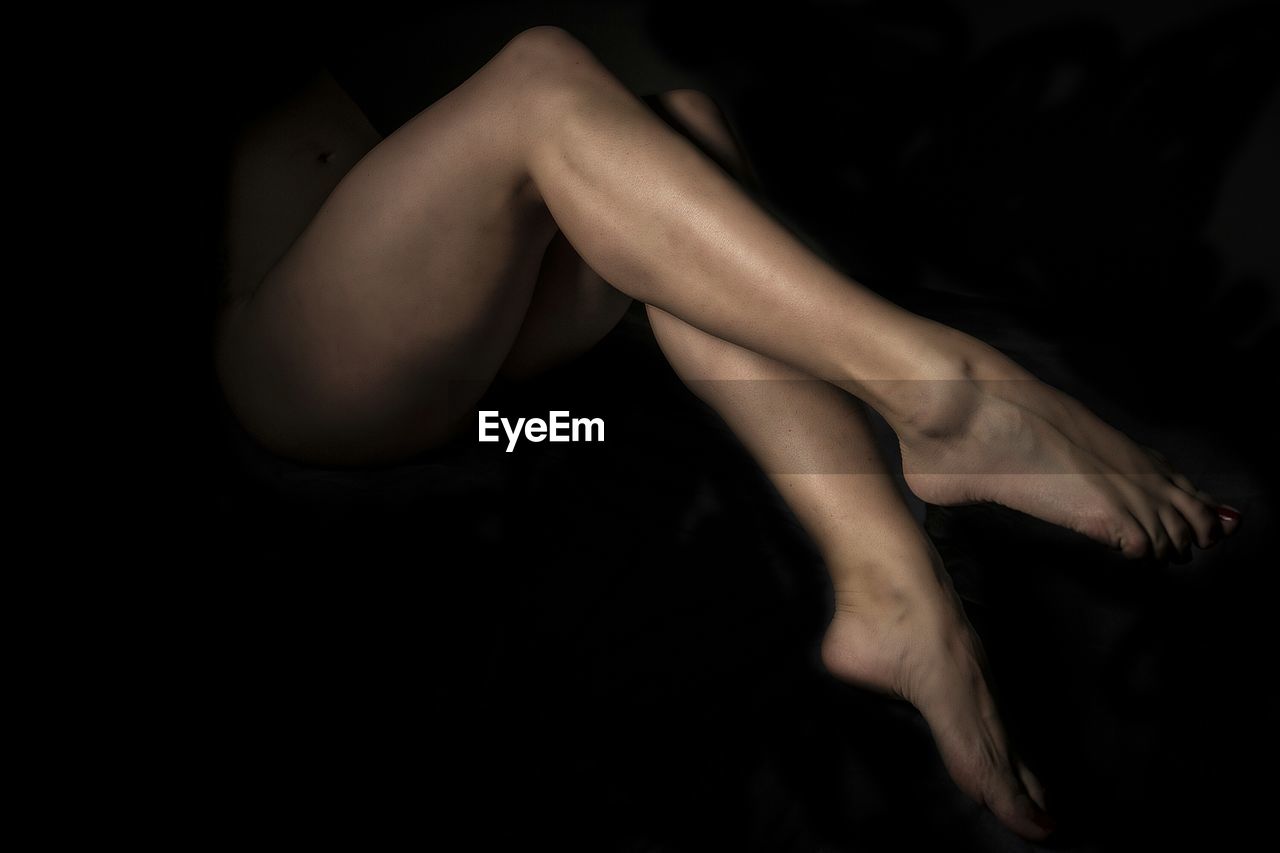 Low section of naked woman against dark background