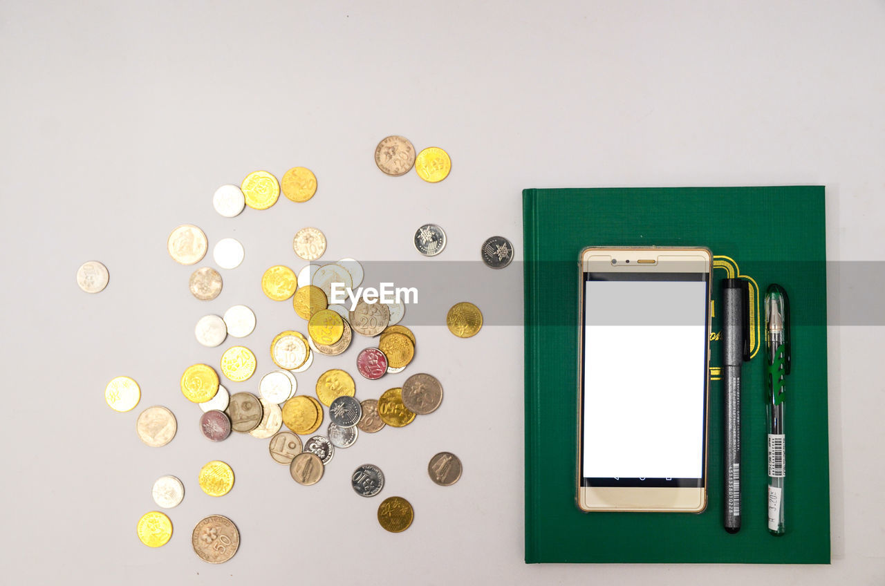 Directly above shot of coins with smart phone and pens against gray background