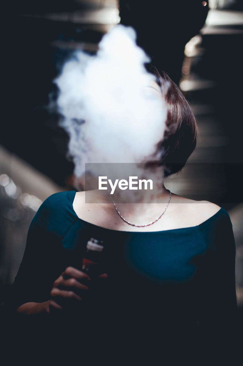 Woman exhaling smoke while holding electronic cigarette