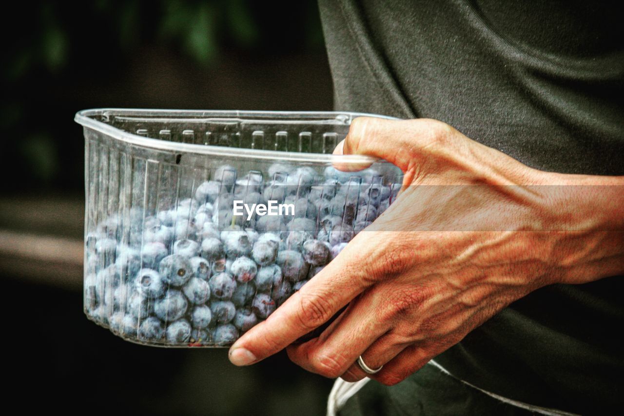 Cropped image of person carrying blueberries in plastic container