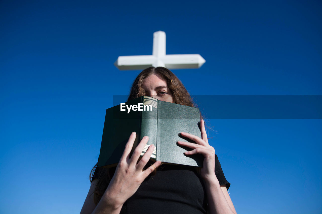 Low angle view of woman holding bible against cross