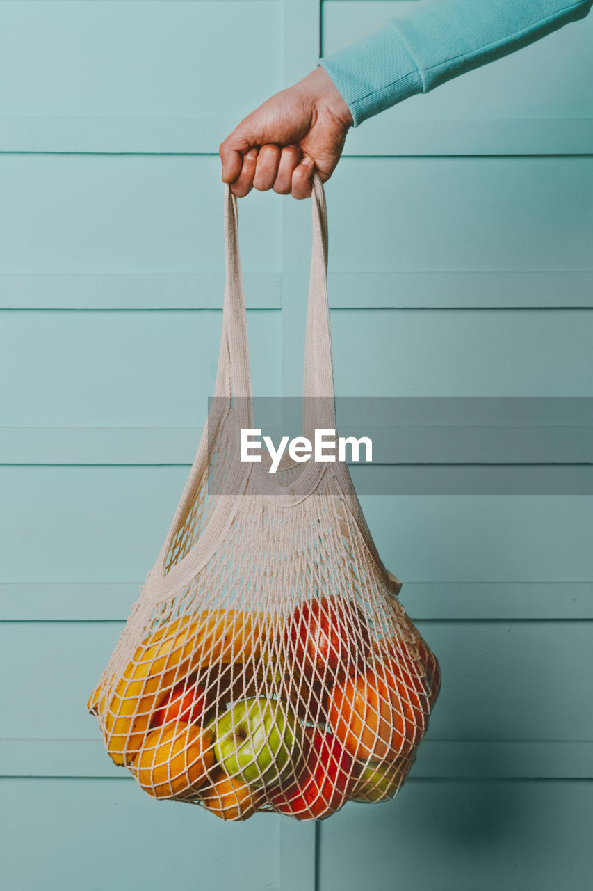 Arm of man holding reusable cotton mesh bag with fresh fruits