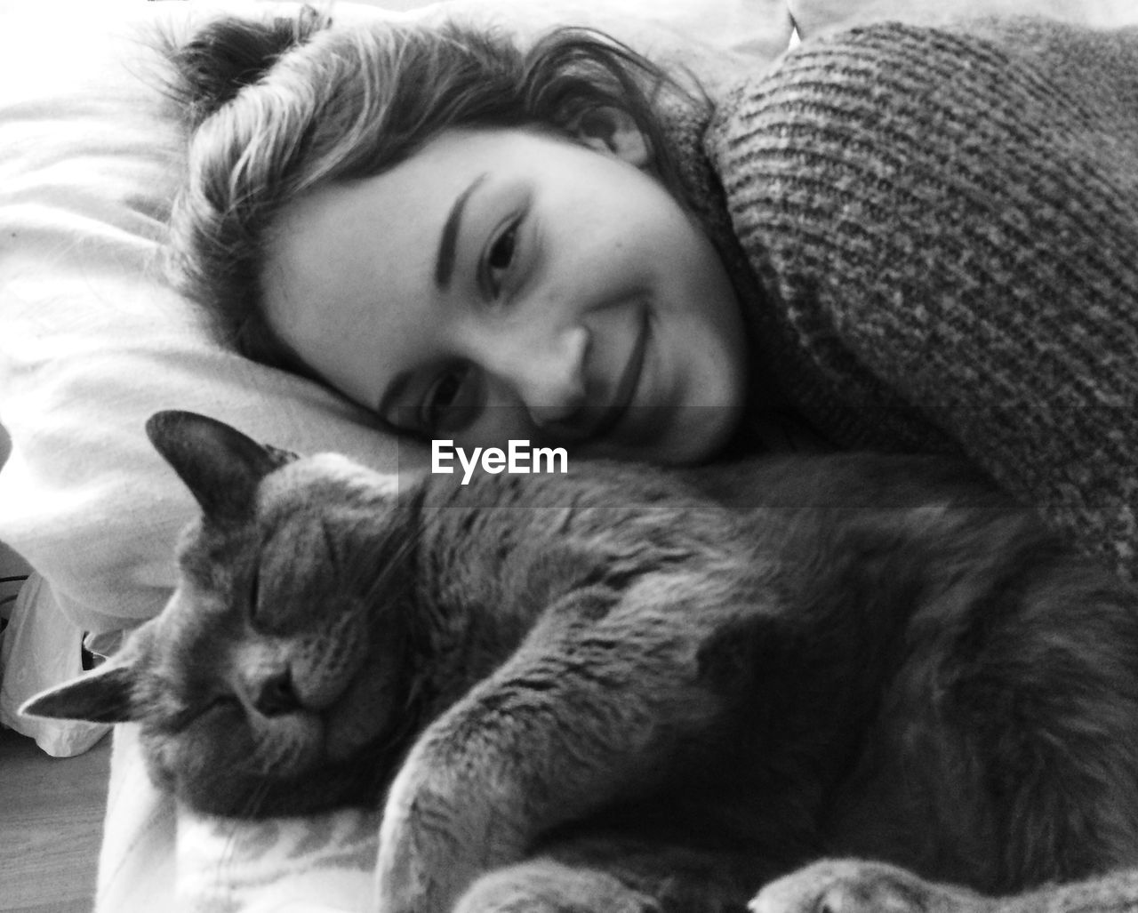 Portrait of beautiful woman lying on bed with cat at home