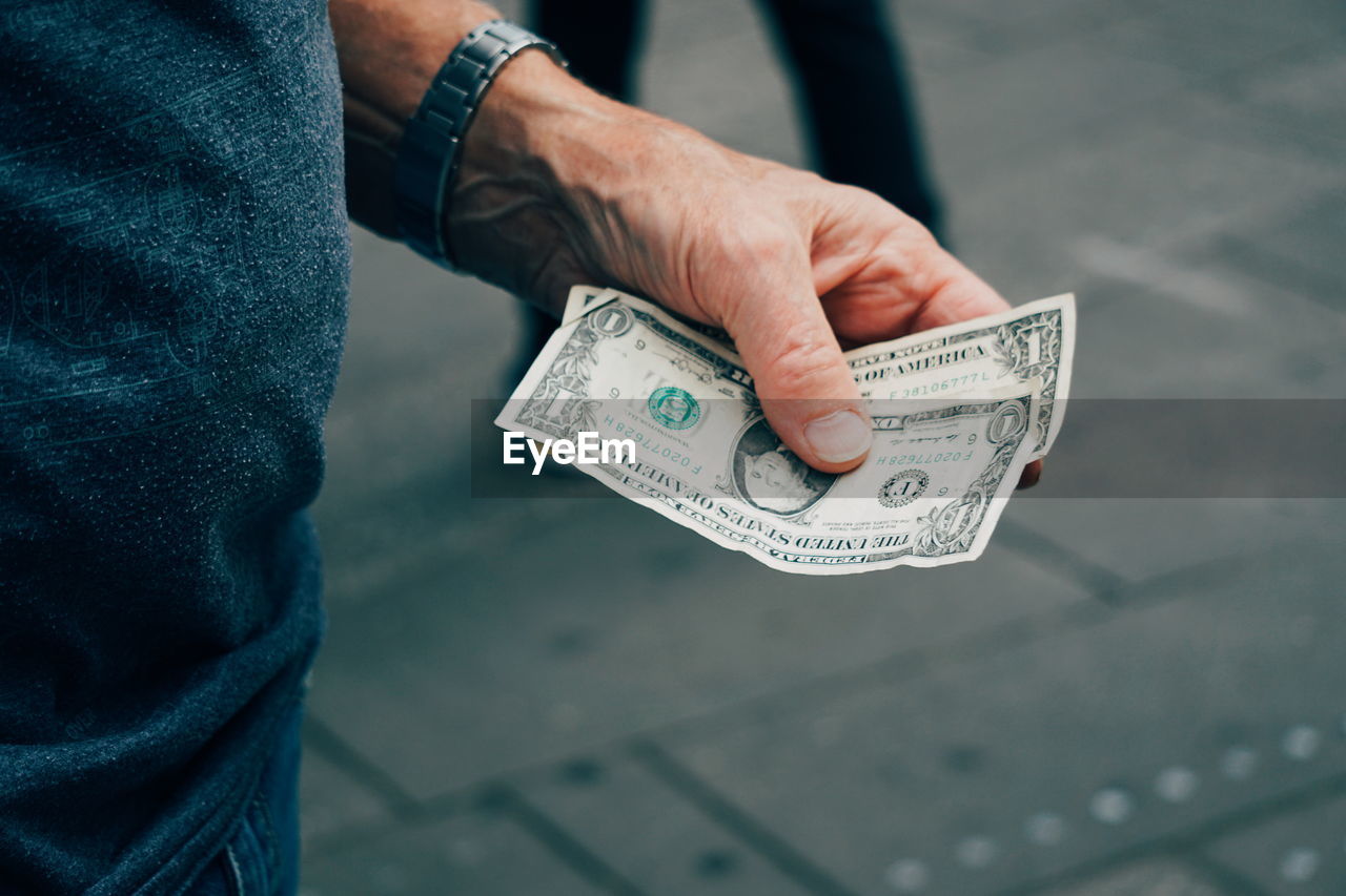 Cropped image of man holding paper currency on street