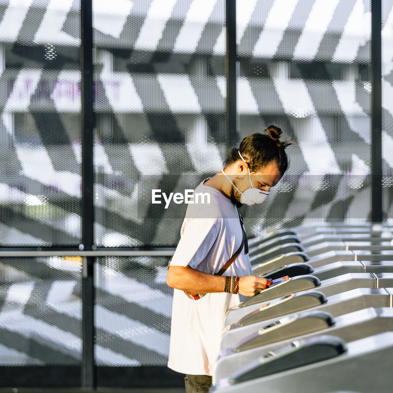 Side view of young man wearing mask making contactless payment at subway station