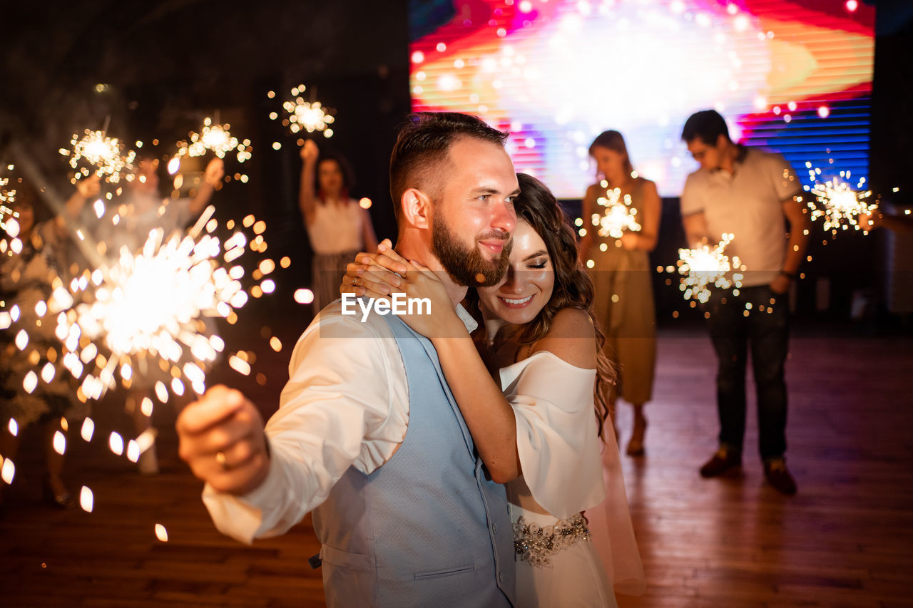 Happy bridegroom holding sparklers at night