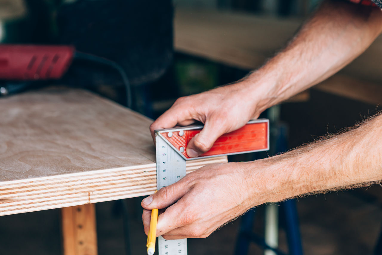 Cropped hands of carpenter measuring wood at workshop