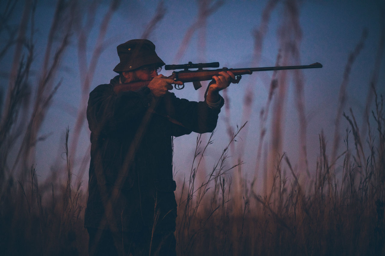Hunter aiming with rifle on grassy field during sunrise