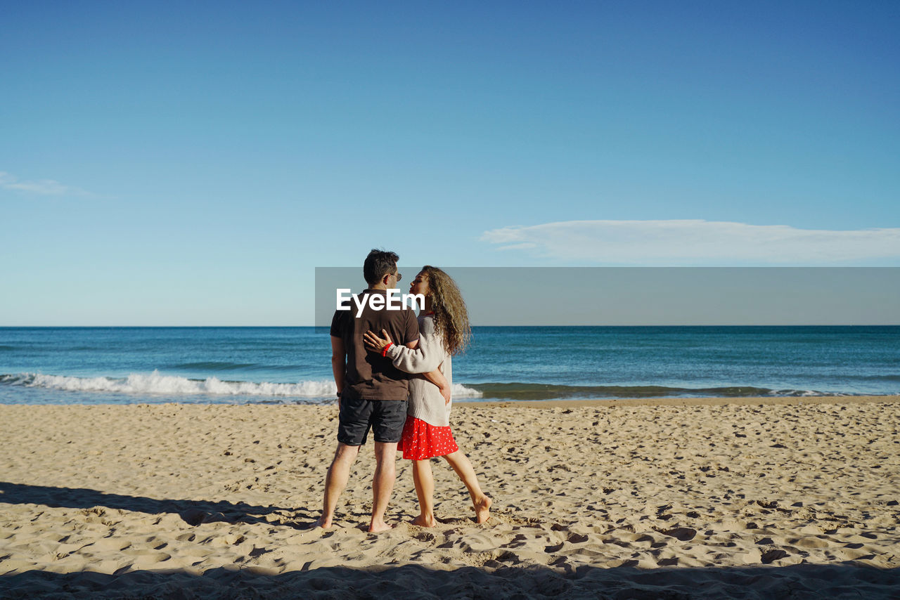 Rear view of woman standing with man  at beach against sky