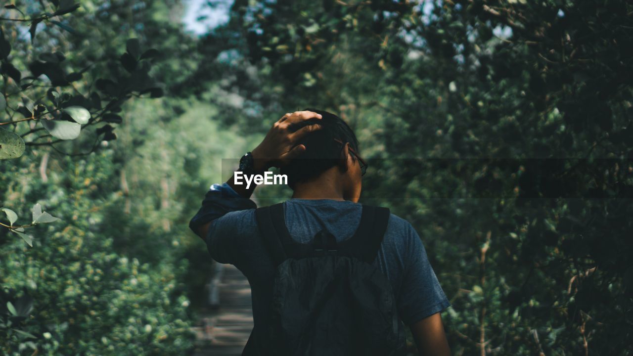 Full length of teenage man standing by tree in forest alone and stressed