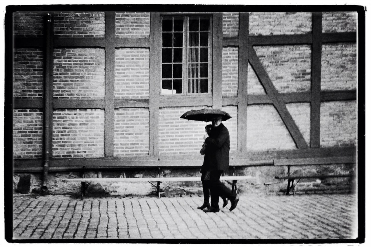 Man and woman sharing umbrella walking on footpath