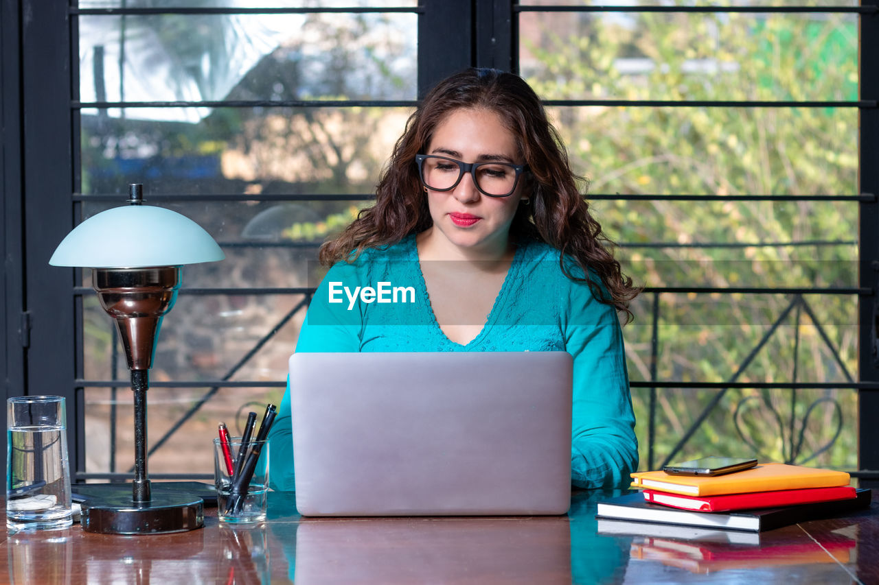 Woman using laptop at desk against window
