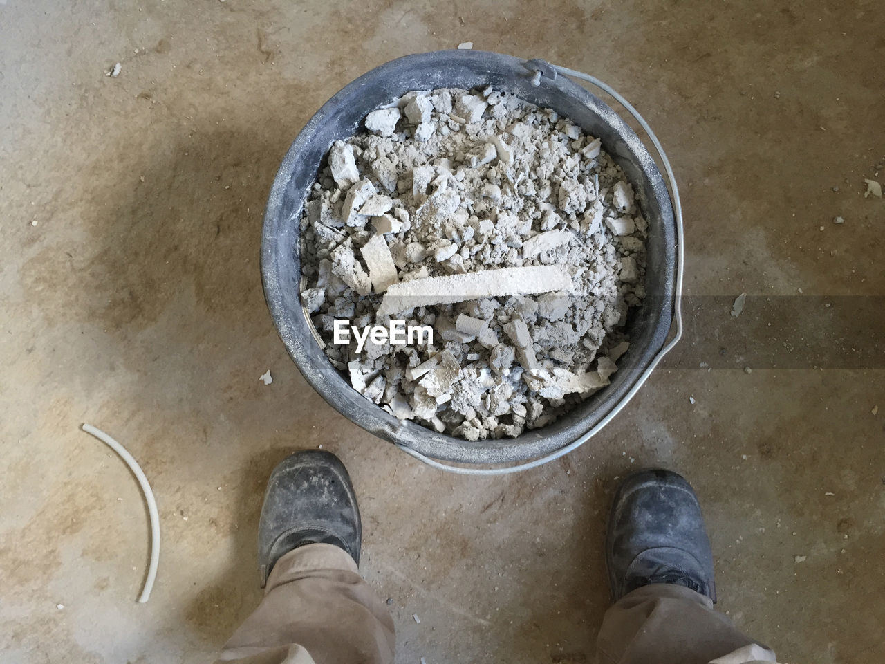 Low section of man standing by broken concrete in bucket on floor