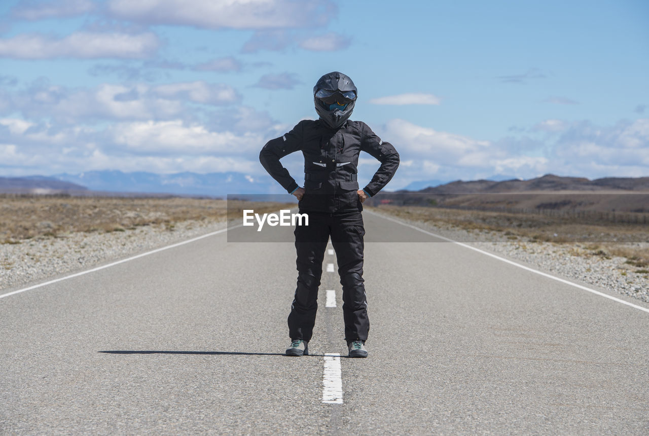 Woman in motorbike gear standing in the middle of empty highway