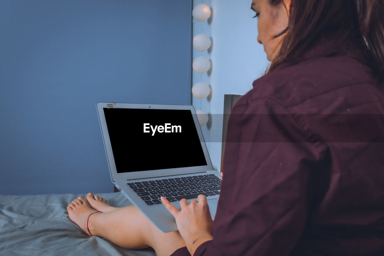 Woman using laptop while sitting on bed at home