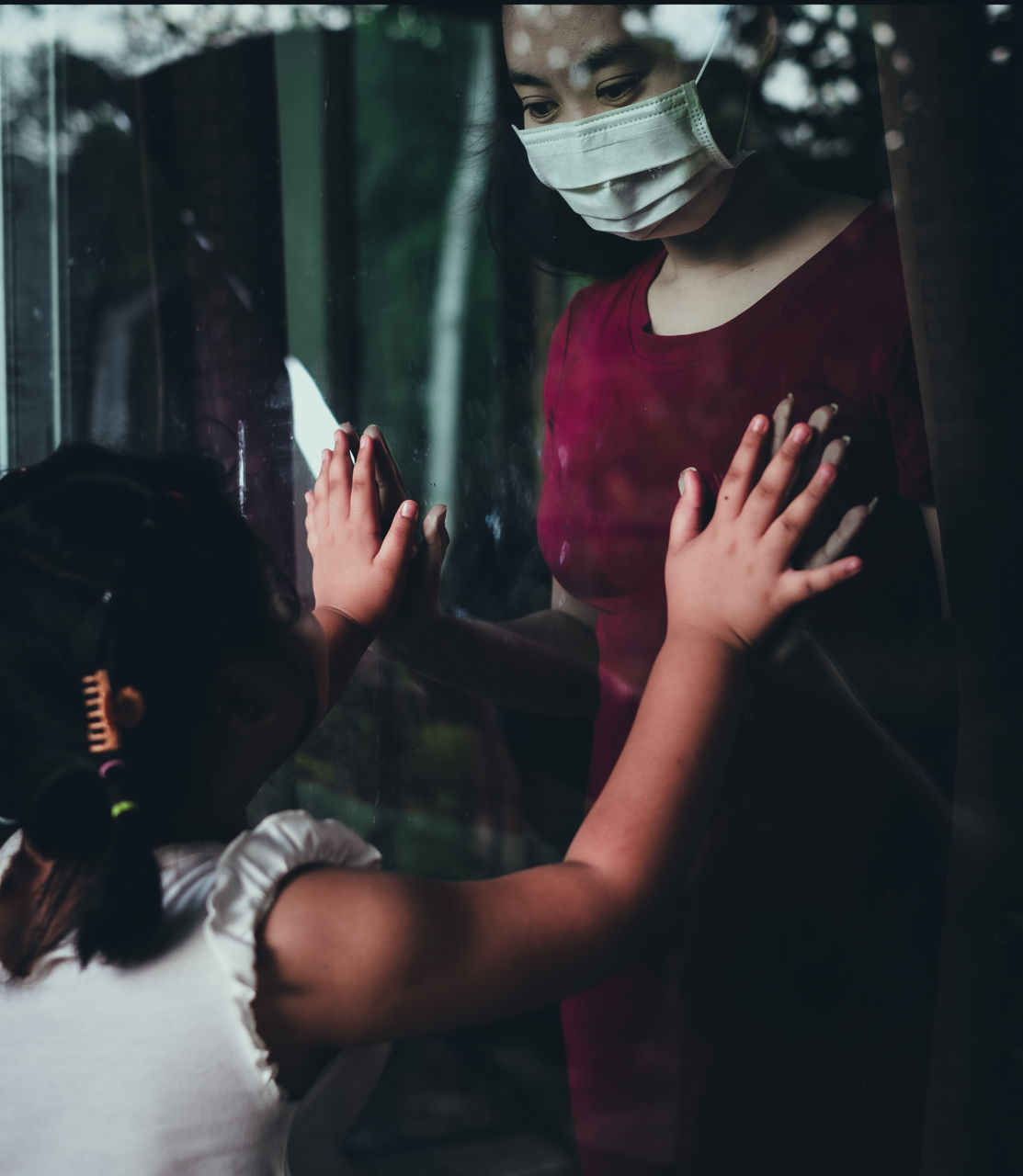 Mother wear face mask meeting daughter and touching hand through the window