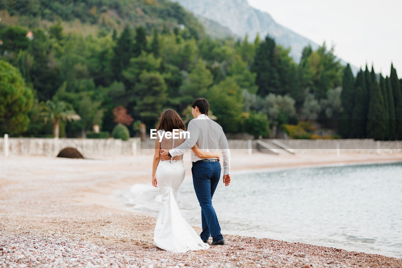 Rear view of couple standing on shore against trees