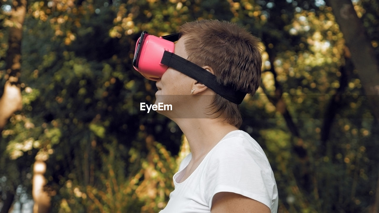 Side view of woman using virtual reality simulator against trees