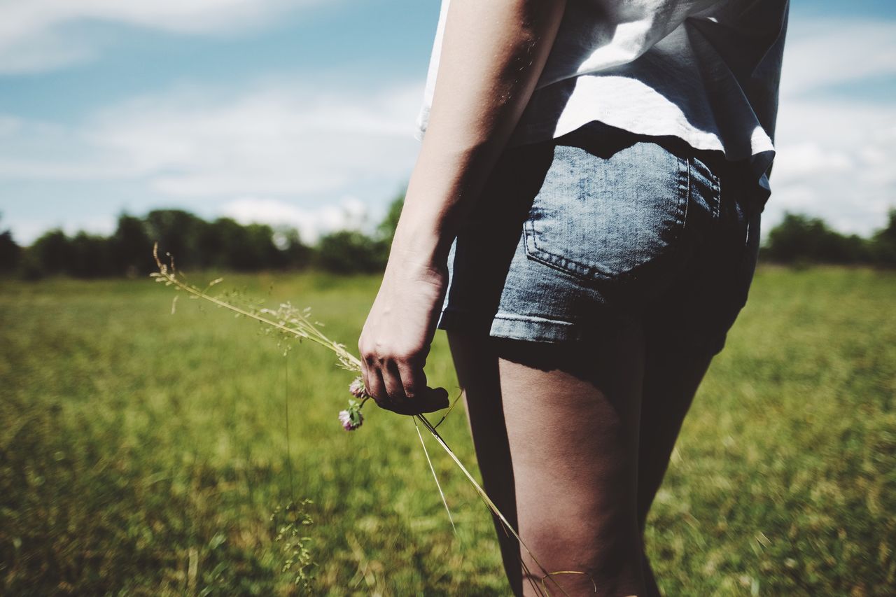 Midsection of woman wearing shorts walking on grassy field