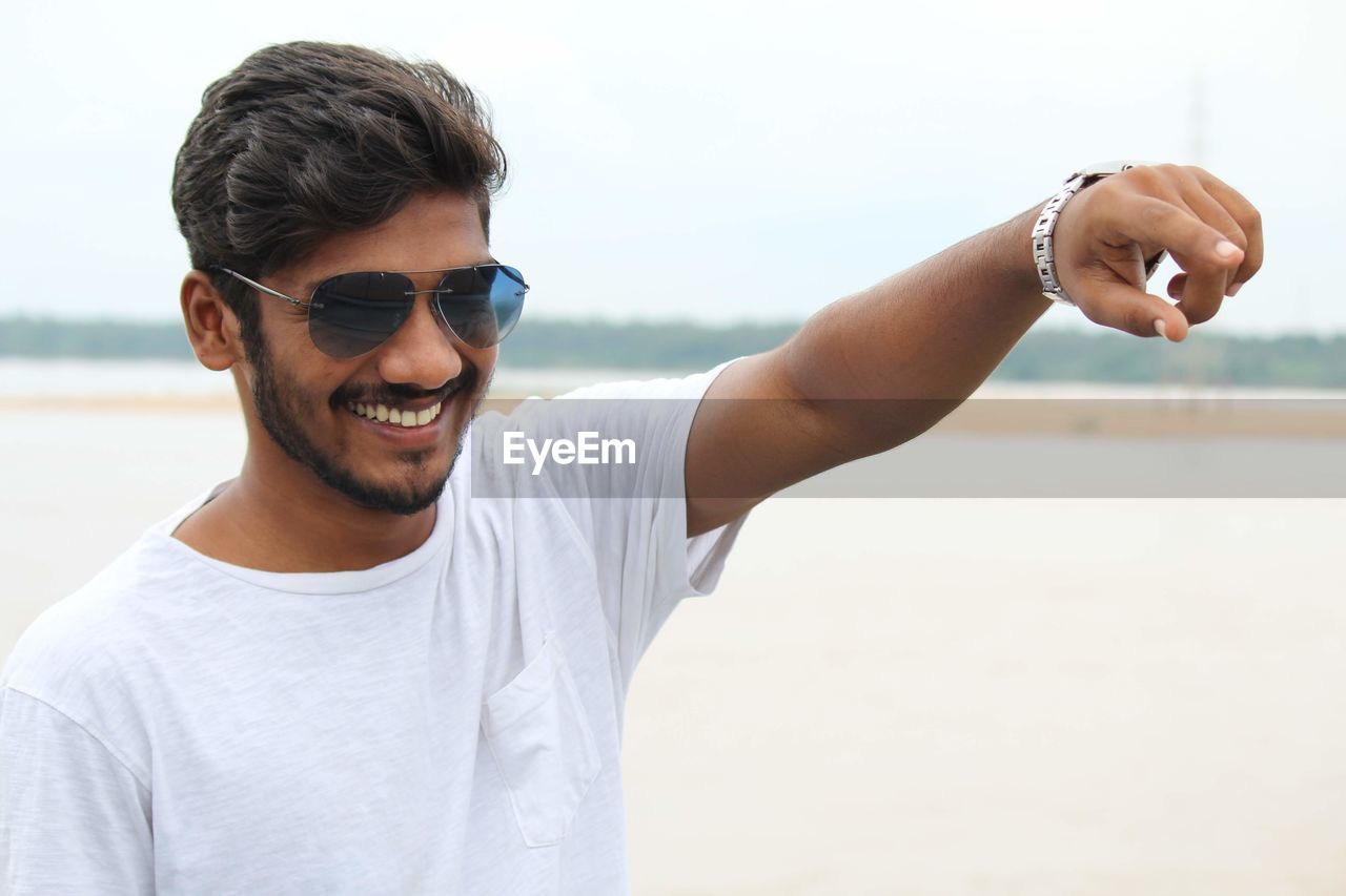 Portrait of young man wearing sunglasses while standing at beach