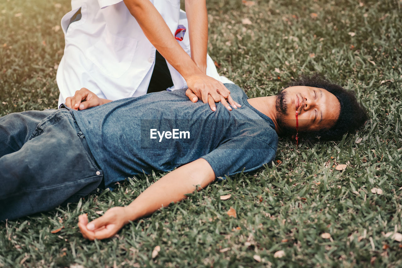 Midsection of doctor performing car on patient lying down at grass outdoors