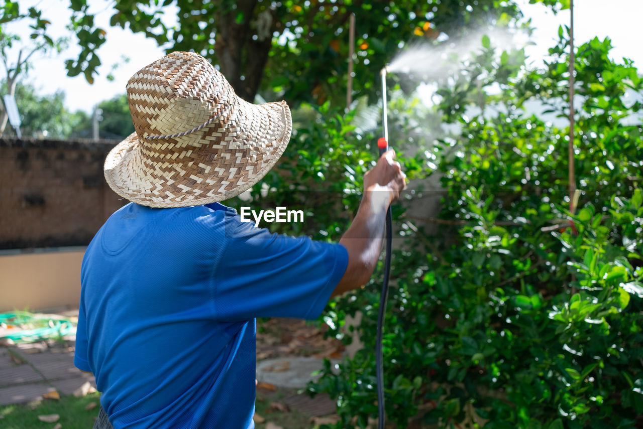 Rear view of man spraying pesticide on plant