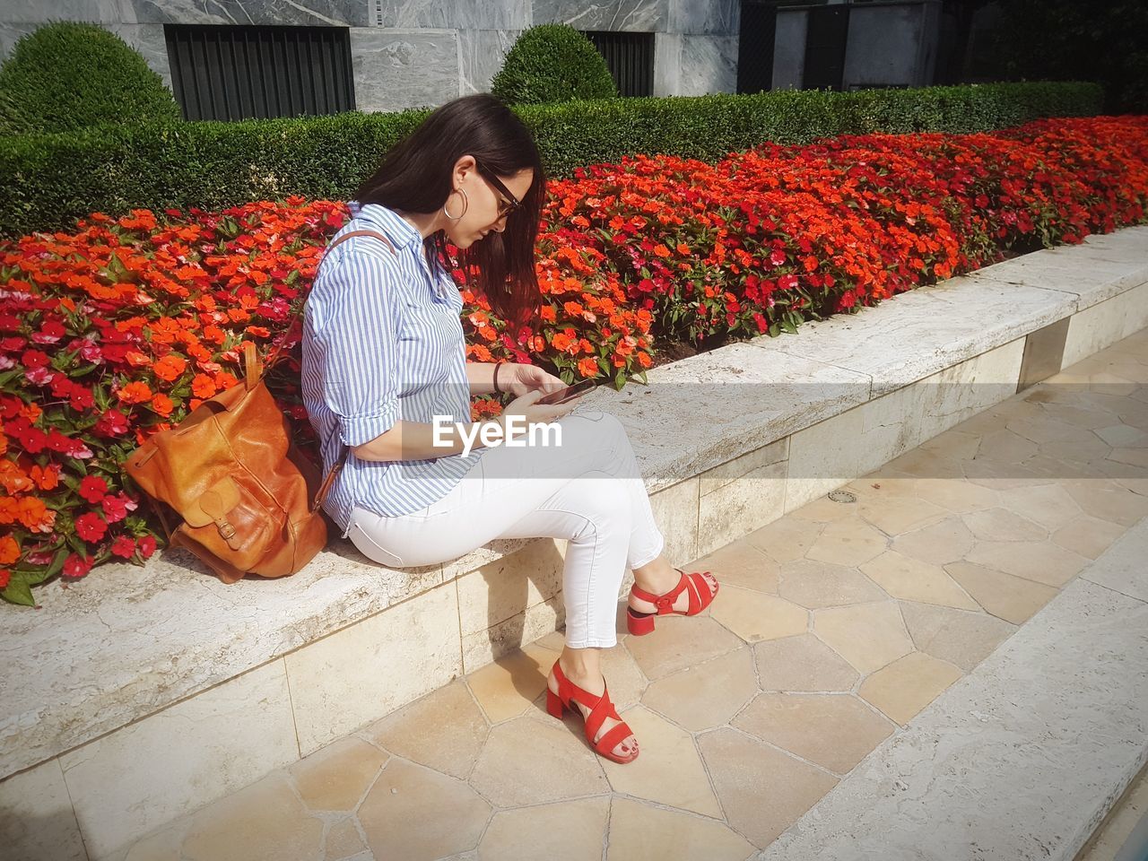 Full length of woman using phone while sitting by flowers