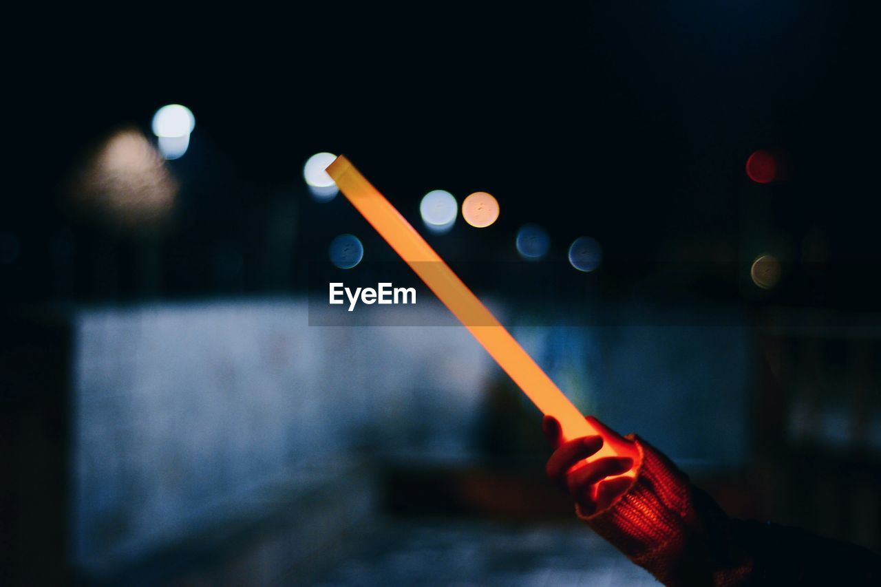 Cropped hand holding laser sword at night