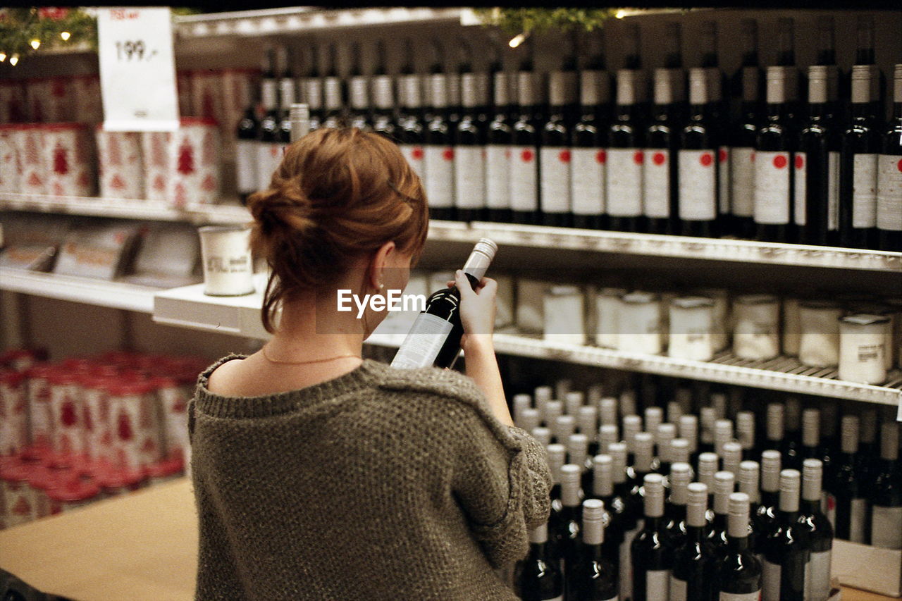 Rear view of woman holding wine bottle at store