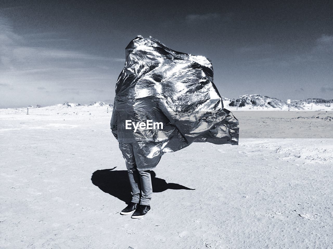 Man covered with silver fabric standing on barren field