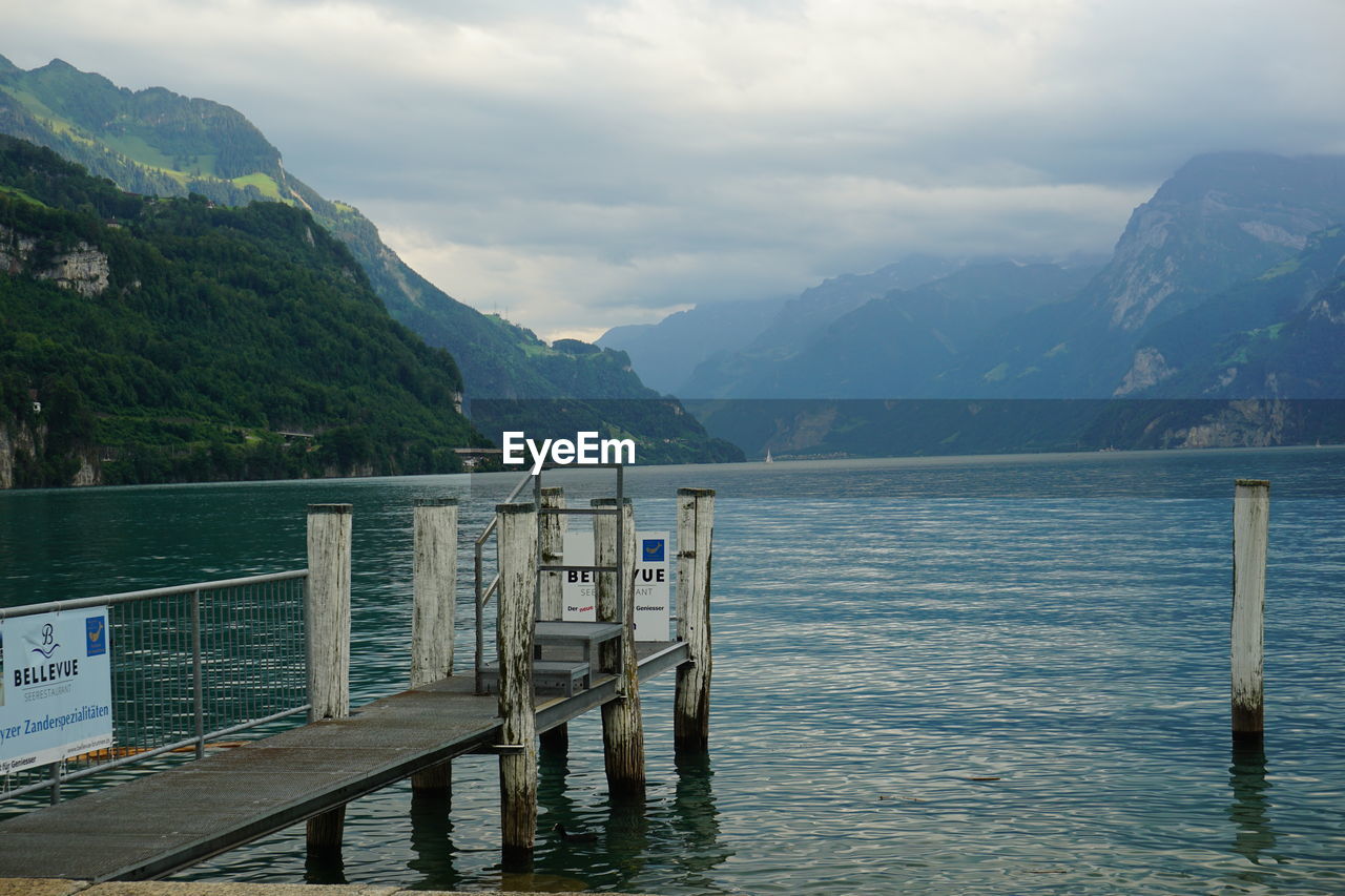 WOODEN POSTS IN LAKE AGAINST MOUNTAINS