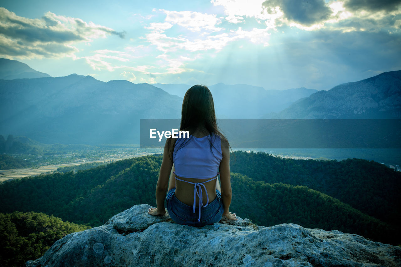 Rear view of woman sitting on rock against mountains
