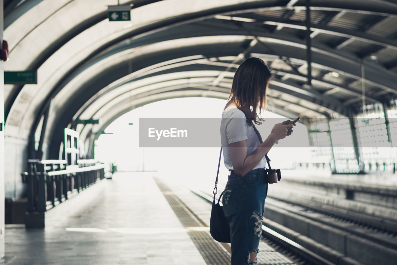 Side view of woman using mobile phone while standing at railroad station platform