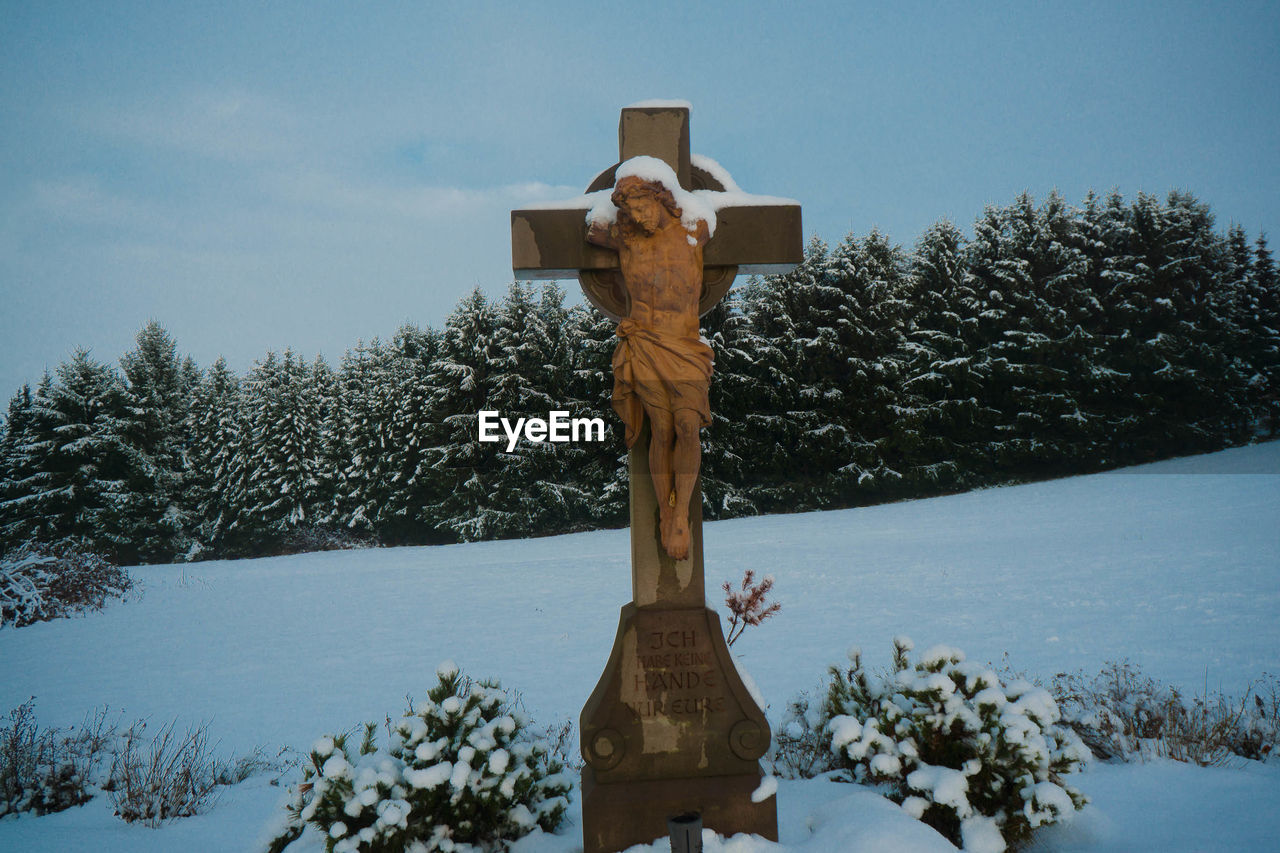 View of cross statue against trees in winter