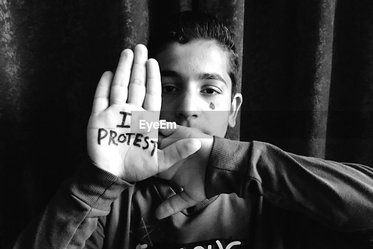 Portrait of teenage boy with i protest text on palm against wall