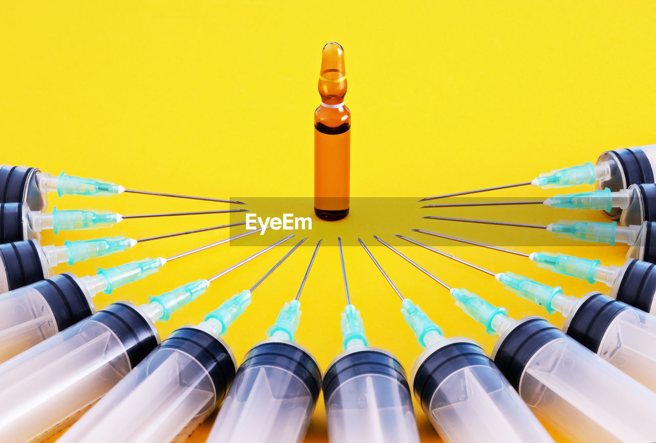 High angle view of syringes and bottle on yellow background