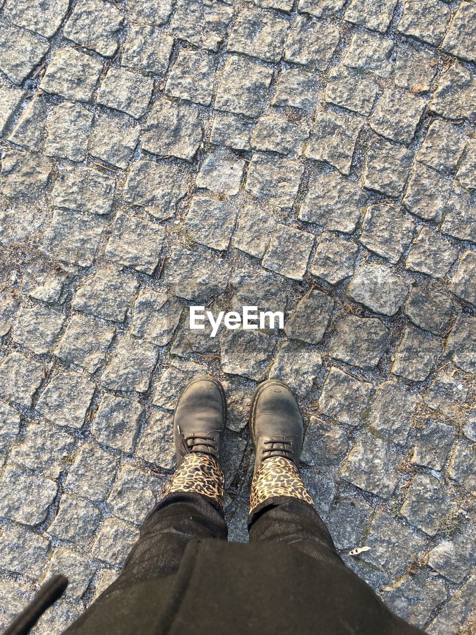 LOW SECTION OF PERSON STANDING ON COBBLESTONE FOOTPATH