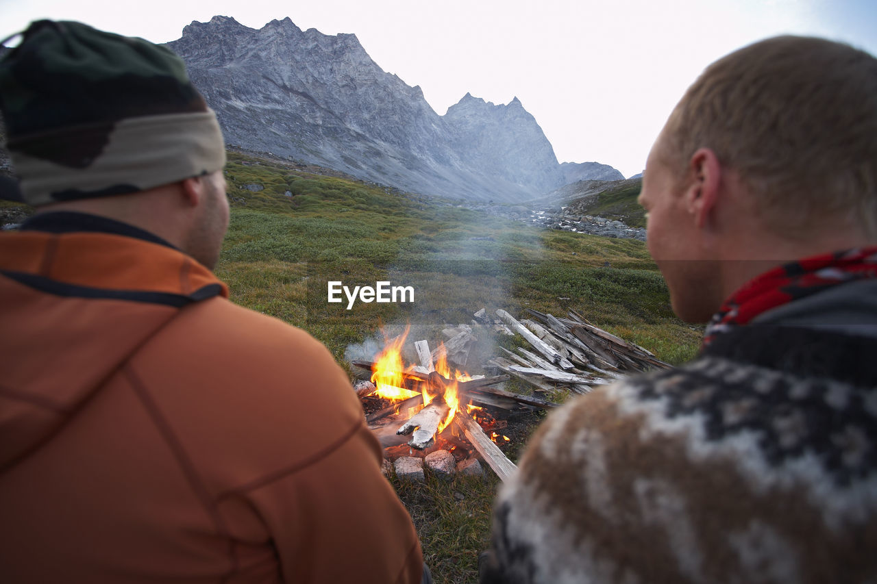 2 male friends sitting at a camp fire in greenland