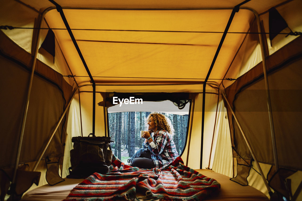 Smiling woman sitting against trees seen through tent