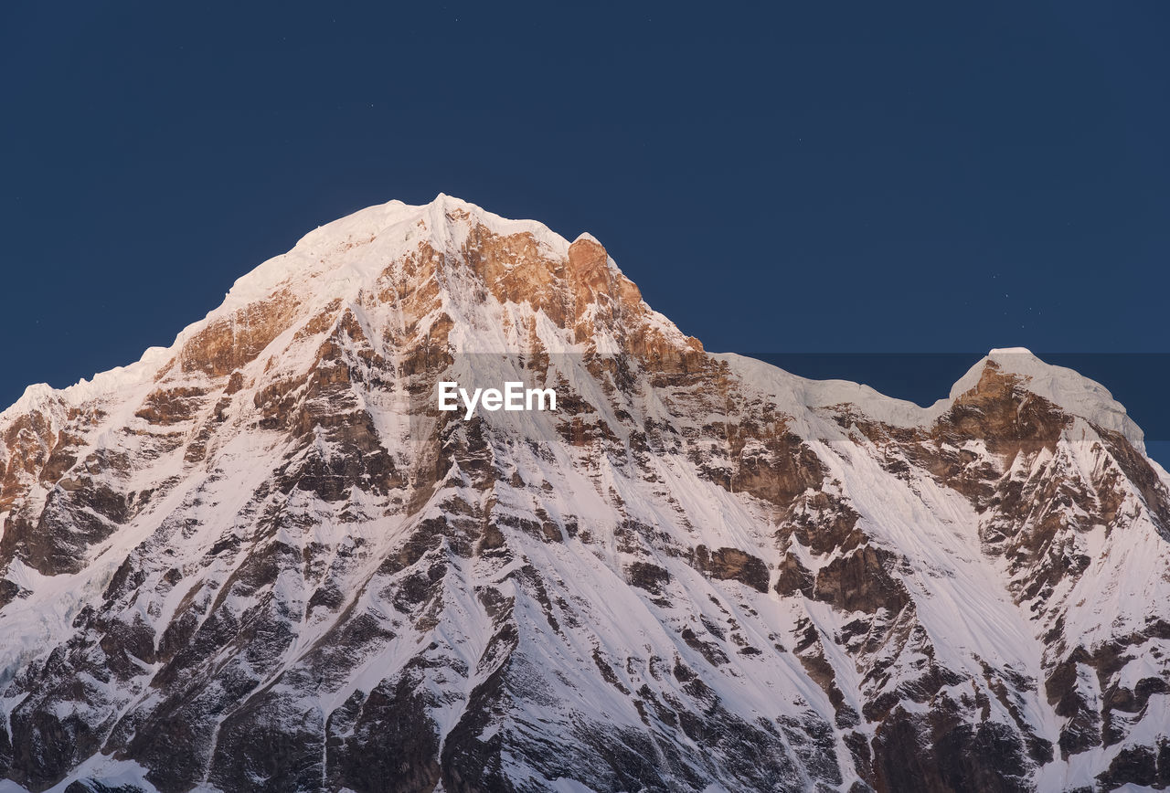 Low angle view of snowcapped mountain against clear sky before sunrise